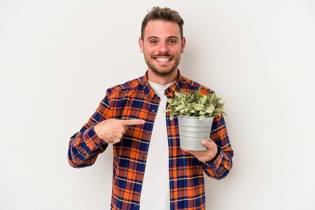 Jonge blanke man met een plant geïsoleerd op een witte achtergrond persoon die met de hand wijst naar een shirt kopieerruimte, trots en zelfverzekerd?
