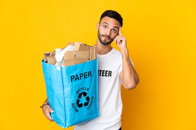 Jonge blanke man met een recycling zak vol papier om te recyclen geïsoleerd op een witte achtergrond, denkend een idee