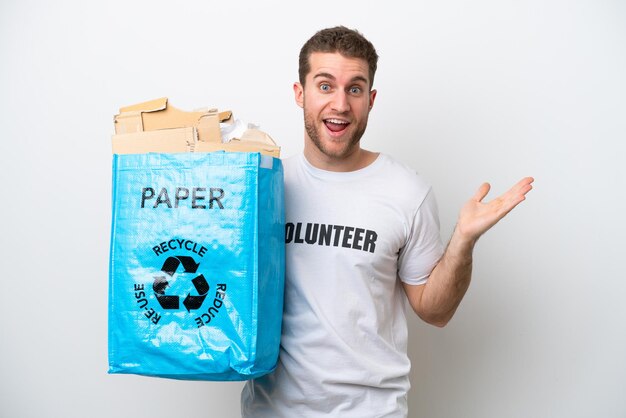 Jonge blanke man met een recycling zak vol papier om te recyclen geïsoleerd op een witte achtergrond met geschokte gelaatsuitdrukking