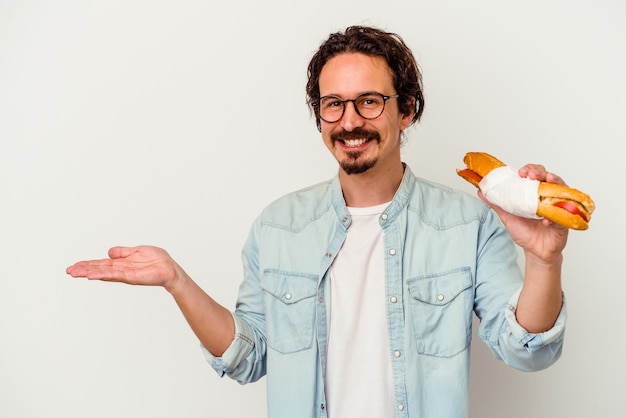 Jonge blanke man met een sandwich geïsoleerd op een witte achtergrond met een kopie ruimte op een palm en met een andere hand op de taille.