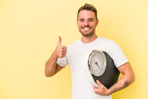 Jonge blanke man met een schaal geïsoleerd op een gele achtergrond glimlachend en duim omhoog