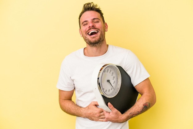 Jonge blanke man met een schaal geïsoleerd op gele achtergrond lachen en plezier hebben.