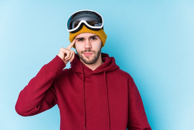 Jonge blanke man met een ski-kleding geïsoleerd wijzende tempel met vinger, denken, gericht op taak.