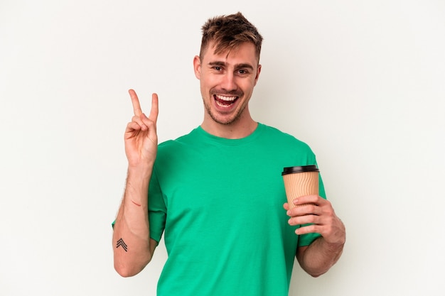 Jonge blanke man met een take-away koffie geïsoleerd op een witte achtergrond vrolijk en zorgeloos met een vredessymbool met vingers.