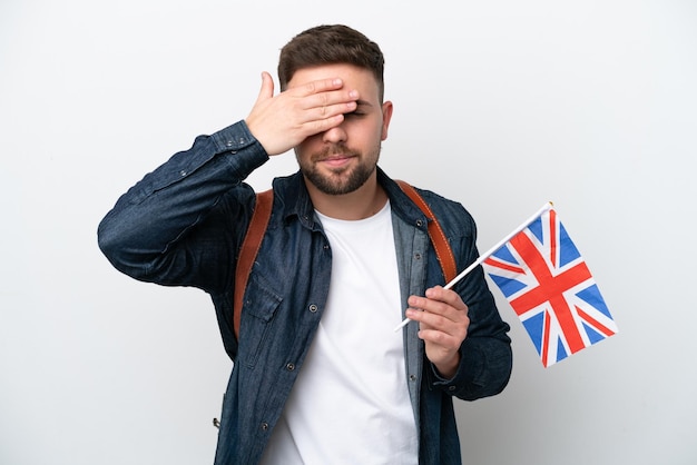 Jonge blanke man met een vlag van het Verenigd Koninkrijk geïsoleerd op een witte achtergrond die ogen bedekt door handen