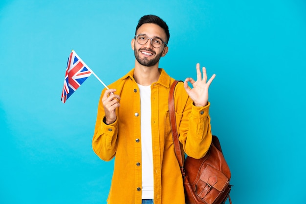 Jonge blanke man met een vlag van het Verenigd Koninkrijk geïsoleerd op gele achtergrond met ok teken met vingers