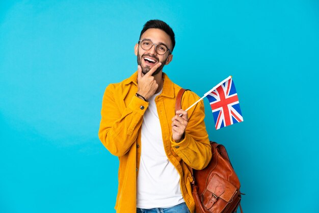Jonge blanke man met een vlag van het Verenigd Koninkrijk geïsoleerd op gele muur blij en lachend