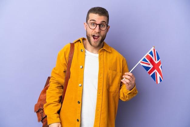 Jonge blanke man met een vlag van het Verenigd Koninkrijk geïsoleerd op paarse muur met verrassingsgelaatsuitdrukking