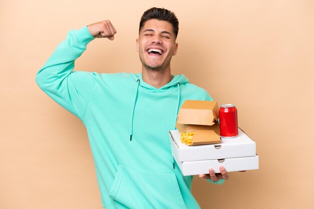 Jonge blanke man met fastfood geïsoleerd op beige achtergrond doet sterk gebaar