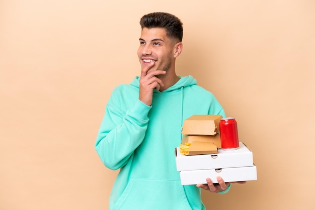 Jonge blanke man met fastfood geïsoleerd op een beige achtergrond terwijl hij glimlacht