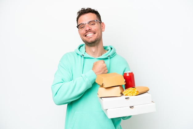 Jonge blanke man met fastfood geïsoleerd op een witte achtergrond die een overwinning viert