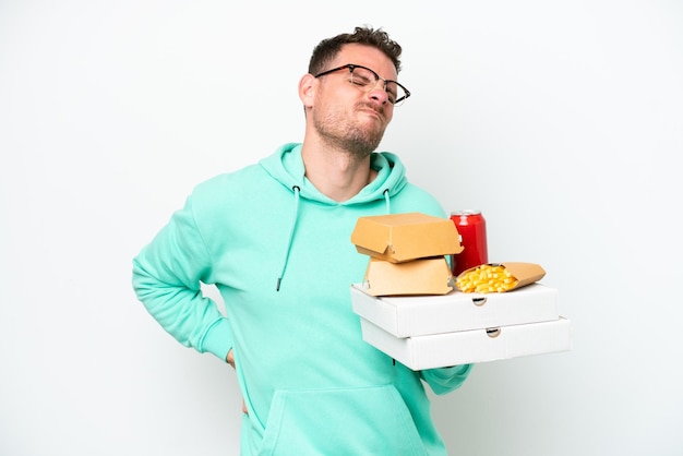 Jonge blanke man met fastfood geïsoleerd op een witte achtergrond die lijdt aan rugpijn omdat hij zich heeft ingespannen