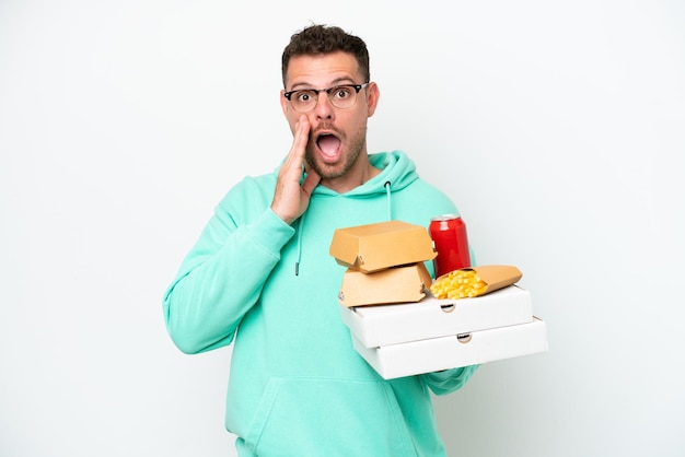 Jonge blanke man met fastfood geïsoleerd op een witte achtergrond met verbazing en geschokte gezichtsuitdrukking