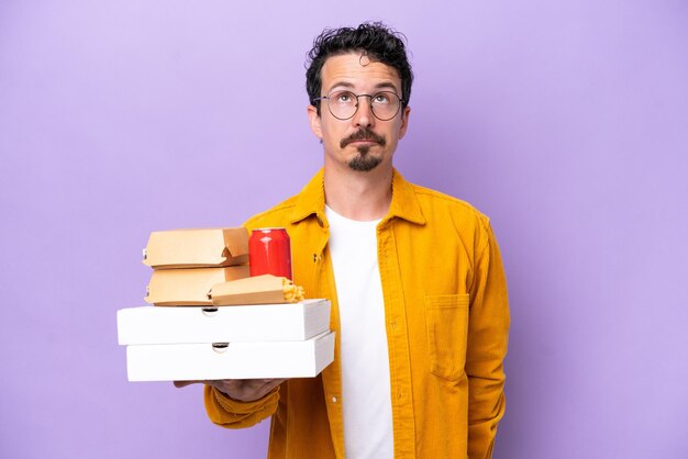 Jonge blanke man met fastfood geïsoleerd op paarse achtergrond en opkijkend