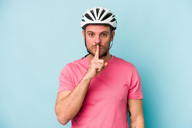 Jonge blanke man met fietshelm geïsoleerd op blauwe achtergrond die een geheim houdt of om stilte vraagt.