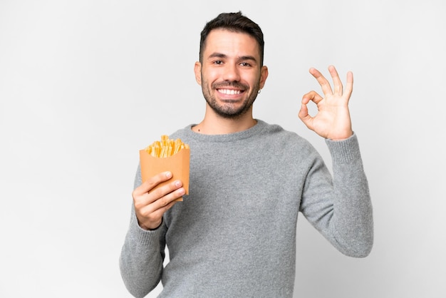 Jonge blanke man met gebakken chips over geïsoleerde witte achtergrond met ok teken met vingers