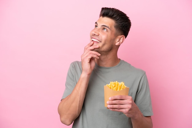 Jonge blanke man met gefrituurde chips geïsoleerd op een roze achtergrond terwijl hij glimlacht