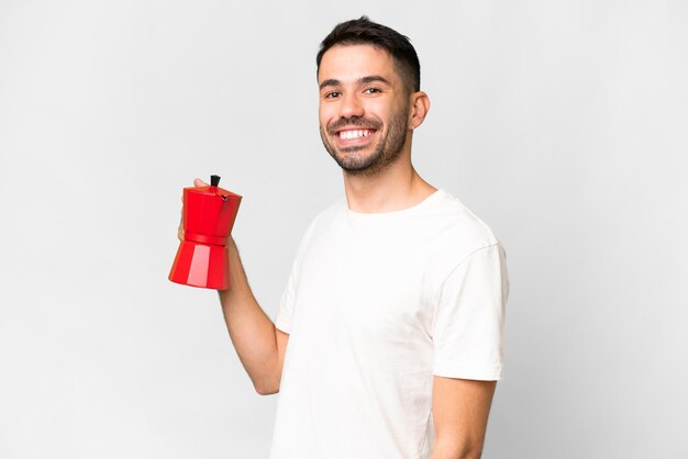 Jonge blanke man met koffiepot over geïsoleerde witte achtergrond die veel lacht