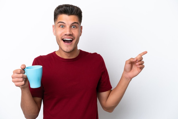Jonge blanke man met kopje koffie geïsoleerd op een witte achtergrond verrast en wijzende vinger naar de zijkant