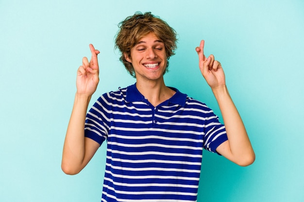 Jonge blanke man met make-up geïsoleerd op een blauwe achtergrond die vingers kruist om geluk te hebben