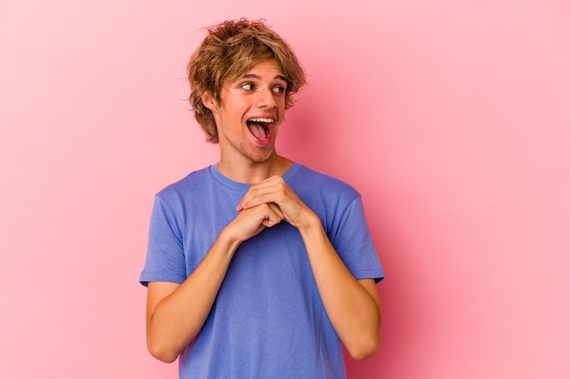 Jonge blanke man met make-up geïsoleerd op roze achtergrond bidden voor geluk, verbaasd en openende mond op zoek naar voren.