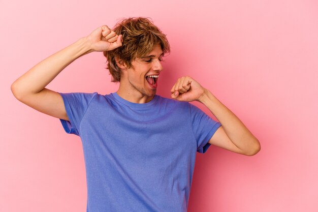 Foto jonge blanke man met make-up geïsoleerd op roze achtergrond die een speciale dag viert, springt en armen opheft met energie.