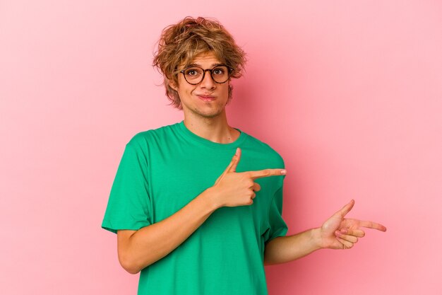 Jonge blanke man met make-up geïsoleerd op roze achtergrond geschokt wijzend met wijsvingers naar een kopieerruimte.