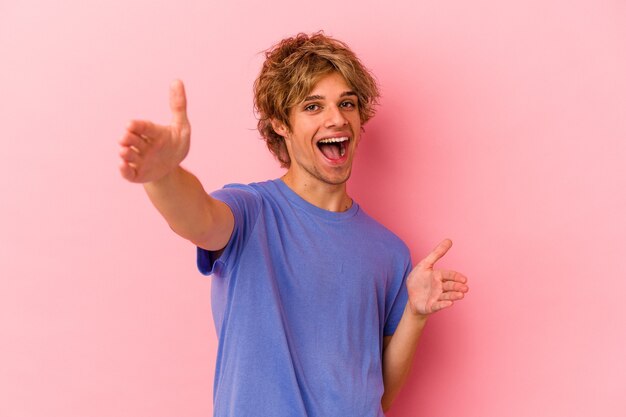 Jonge blanke man met make-up geïsoleerd op roze achtergrond voelt zich zelfverzekerd en geeft een knuffel aan de camera.