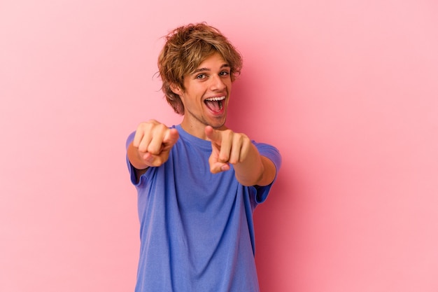 Jonge blanke man met make-up geïsoleerd op roze achtergrond wijzend naar voren met vingers.