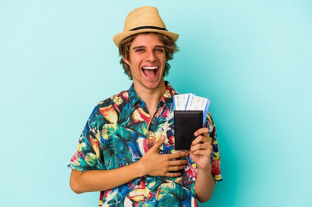 Jonge blanke man met make-up met paspoort geïsoleerd op blauwe achtergrond lachen en plezier hebben.