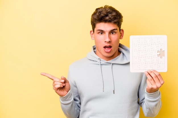 Jonge blanke man met puzzel geïsoleerd op een gele achtergrond die naar de zijkant wijst