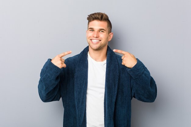 Jonge blanke man met pyjama glimlacht, wijzende vingers op de mond.