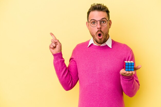 Jonge blanke man met Rubik's kubus geïsoleerd op een gele achtergrond die naar de zijkant wijst