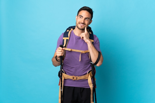 Jonge blanke man met rugzak en wandelstokken geïsoleerd op blauw een idee denken tijdens het opzoeken