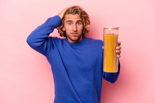 Jonge blanke man met spaghetti pot geïsoleerd op roze achtergrond geschokt, ze heeft een belangrijke vergadering onthouden.