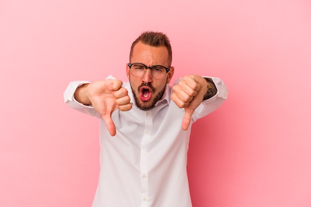 Jonge blanke man met tatoeages geïsoleerd op roze achtergrond duim omlaag tonen en afkeer uiten.