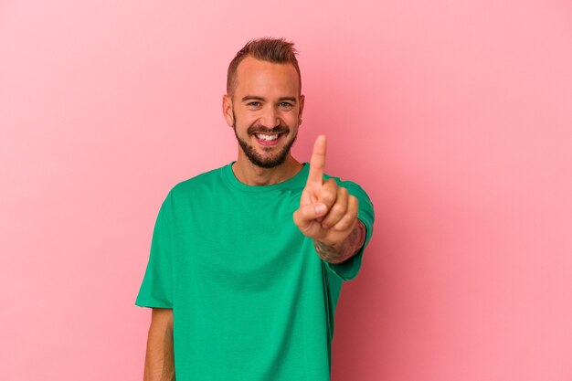 Jonge blanke man met tatoeages geïsoleerd op roze achtergrond met nummer één met vinger.