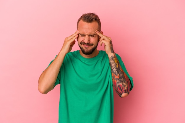 Jonge blanke man met tatoeages geïsoleerd op roze achtergrond tempels aan te raken en hoofdpijn te hebben.