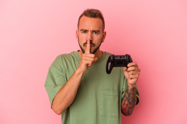 Jonge blanke man met tatoeages met gamecontroller geïsoleerd op roze achtergrond die een geheim houdt of om stilte vraagt.