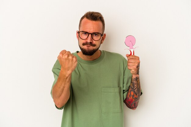 Jonge blanke man met tatoeages met lolly geïsoleerd op een witte achtergrond met vuist naar camera, agressieve gezichtsuitdrukking.