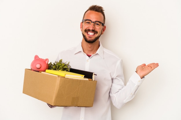 Jonge blanke man met tatoeages verhuizen naar huis geïsoleerd op een witte achtergrond met een kopie ruimte op een palm en met een andere hand op de taille.