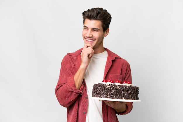 Jonge blanke man met verjaardagstaart over geïsoleerde achtergrond naar de zijkant kijkend en glimlachend