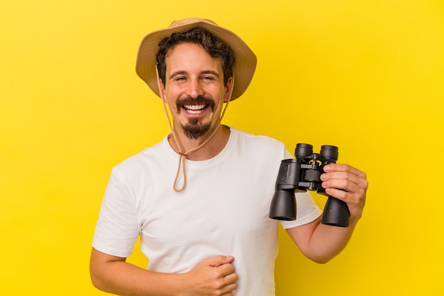 Jonge blanke man met verrekijker geïsoleerd op gele achtergrond lachen en plezier hebben.