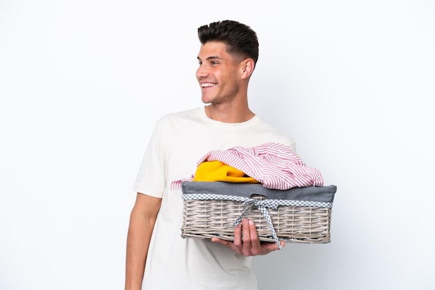 Jonge blanke man met wasmand geïsoleerd op een witte achtergrond, opzij kijkend en glimlachend