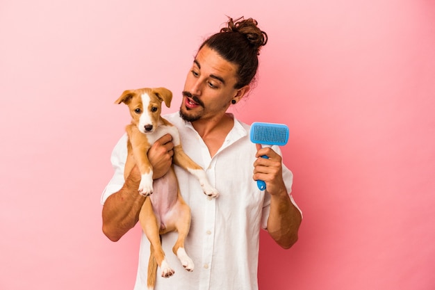 Jonge blanke man met zijn puppy en hond borstel geïsoleerd op roze achtergrond