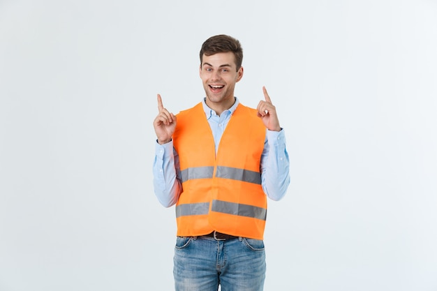 Jonge blanke man op witte achtergrond met aannemersuniform en veiligheidshelm verrast met een idee of vraag wijzende vinger met blij gezicht, nummer één.