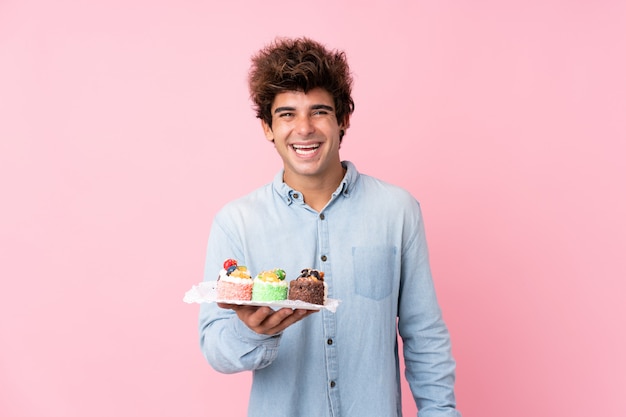 Jonge blanke man over geïsoleerde roze muur met mini cakes