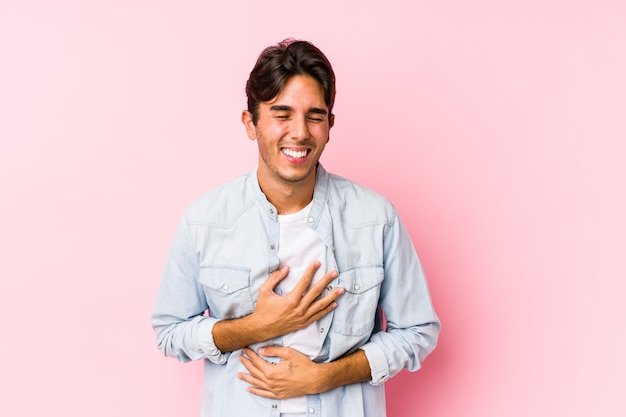 Jonge blanke man poseren in een roze achtergrond geïsoleerd lacht vrolijk en heeft plezier met handen op de buik.