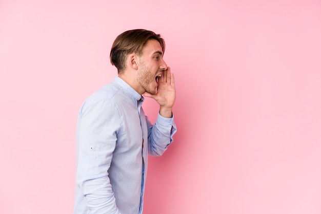 Jonge blanke man poseren in een roze muur geïsoleerd schreeuwen en houden palm in de buurt van geopende mond.