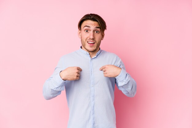 Jonge blanke man poseren in een roze muur verrast wijzend met vinger, breed glimlachend.